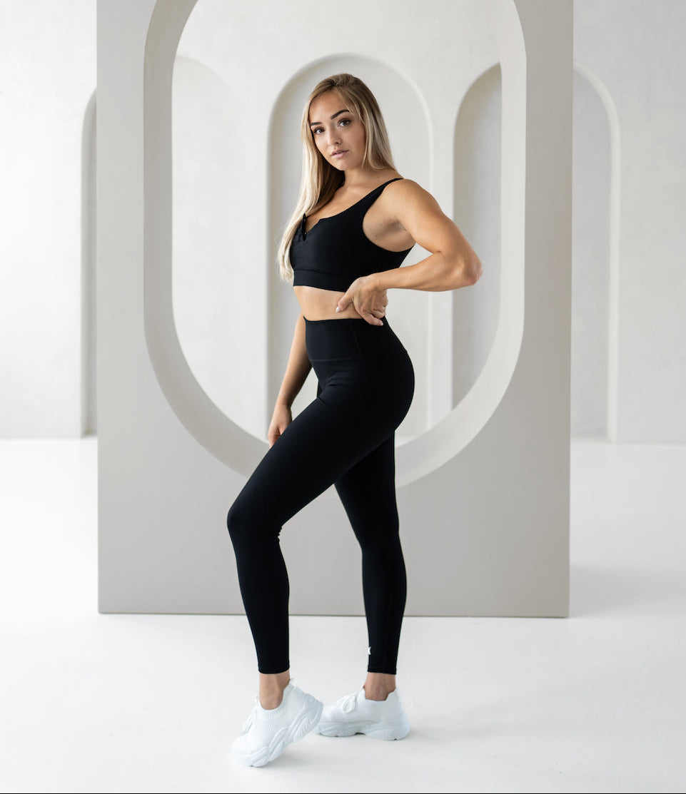 Woman in black athletic wear standing in front of a white wall with geometric arches.
