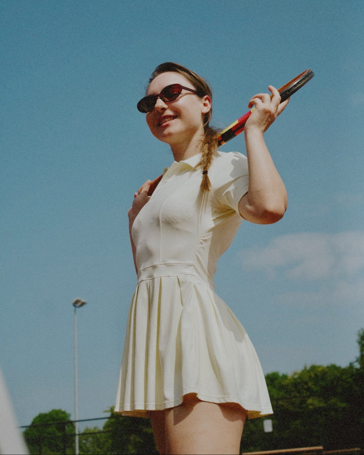 Woman in a vintage tennis outfit holding a racket against a blue sky.